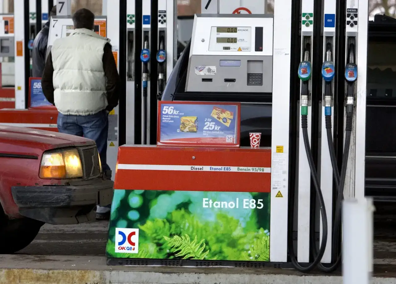 Vid en bensinstation fyller en person p&aring; sin r&ouml;da bil. En pump visar 