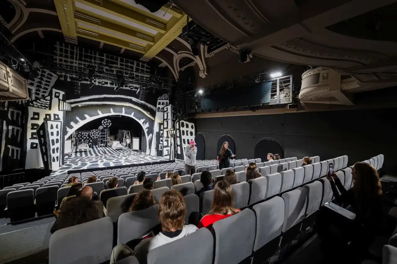 Widownia teatru z widokiem na scenę w stylu modernizmu, z czarno-białą scenografią przypominającą miejski krajobraz.