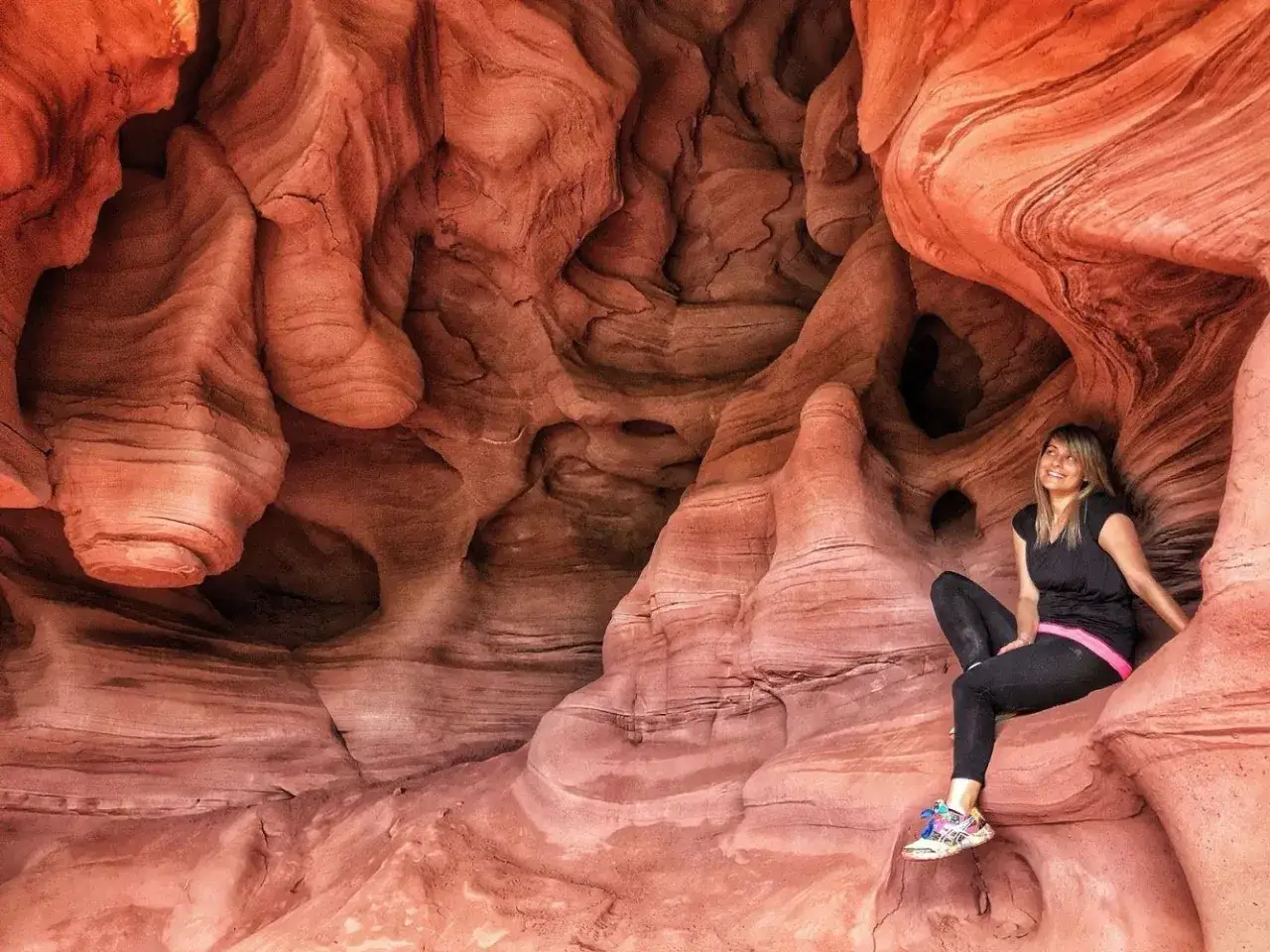 Una mujer sonr&iacute;e sentada en las impresionantes formaciones rocosas de las coves de Can Riera, un lugar m&aacute;gico esculpido por el tiempo.