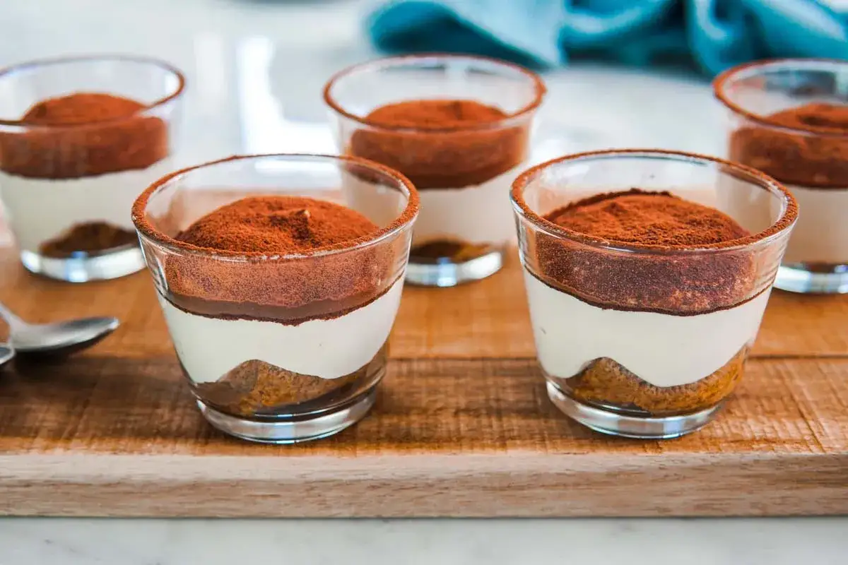 Deliziosi bicchierini di tiramisù senza uova, con strati di crema soffice, savoiardi inzuppati e abbondante cacao amaro in polvere.