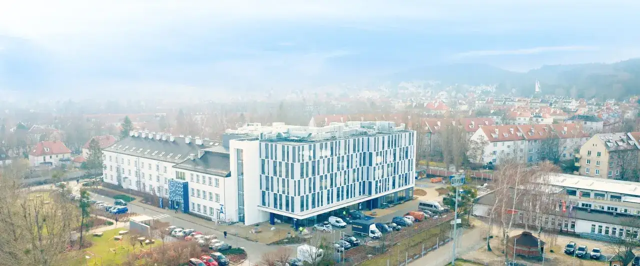 Nowoczesny budynek WSB Gdańsk z charakterystyczną fasadą, otoczony zabudową miejską i zielenią.