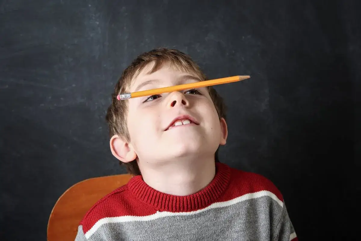 Chłopiec z ołówkiem na nosie, być może jedna z oznak ADHD, patrzy w górę z uśmiechem.