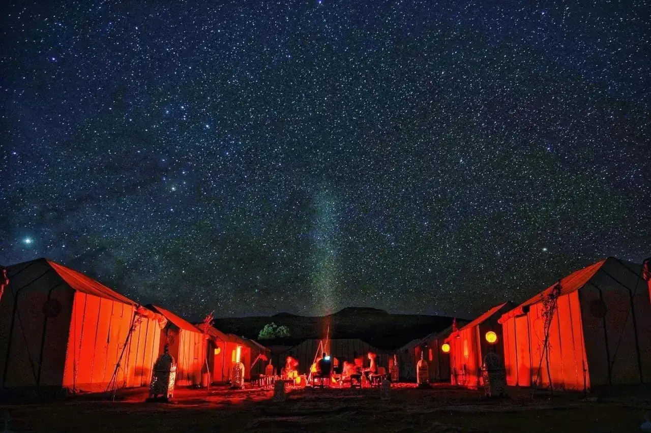 Campement dans le désert du Sahara sous un ciel étoilé. La température du désert sahara la nuit est fraîche, contrastant avec la chaleur des tentes illuminées.