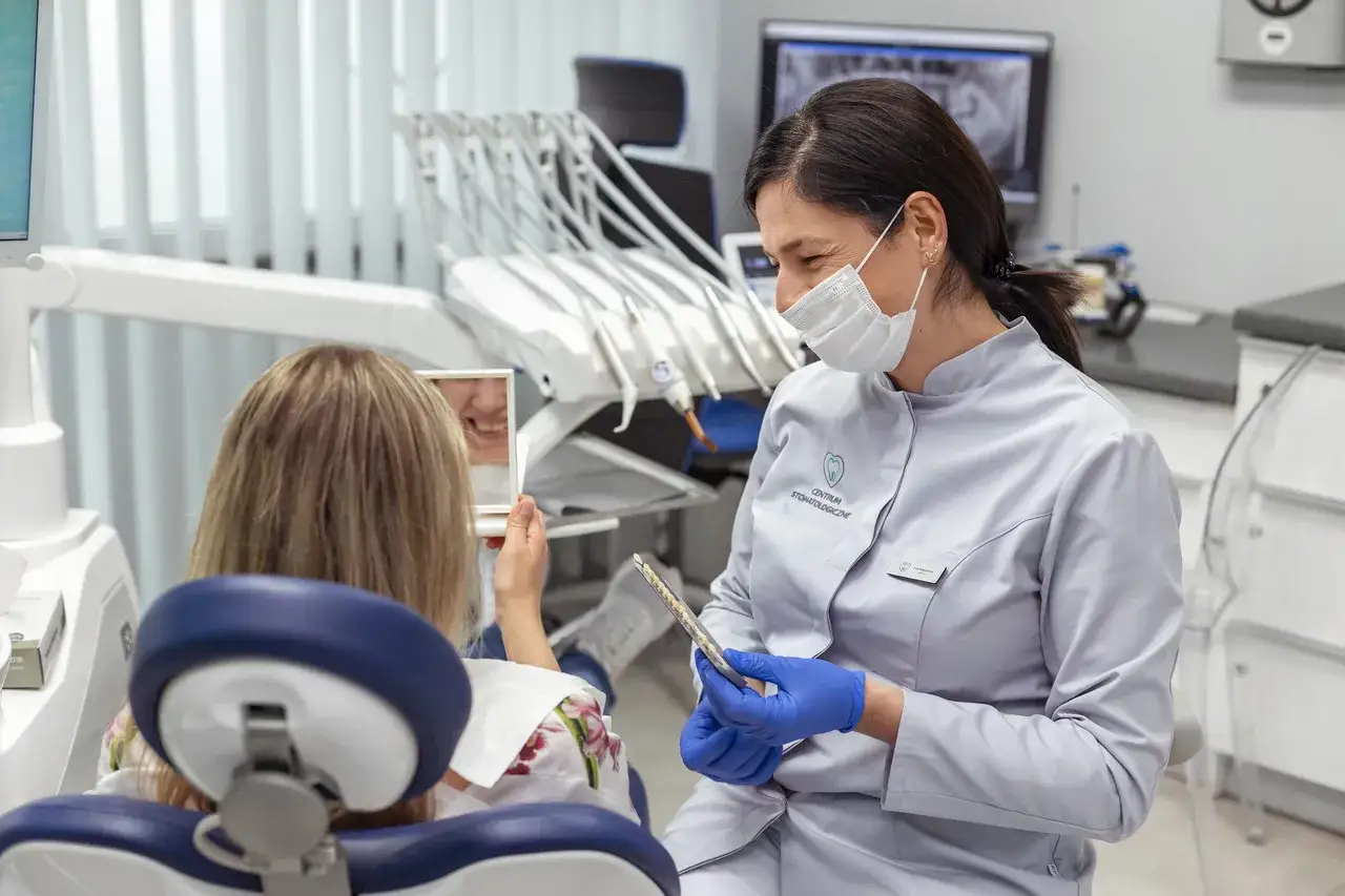 Dentystka pokazuje pacjentce wzornik kolor&oacute;w, odpowiadając na pytanie: czy plomba może wypaść. Pacjentka ogląda sw&oacute;j uśmiech w lusterku.