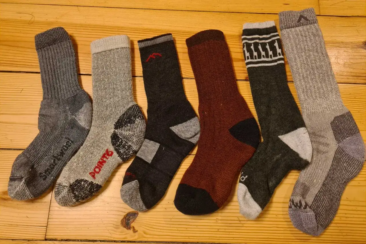 Six paires de chaussettes de randonn&eacute;e, de diff&eacute;rentes couleurs et motifs, sont align&eacute;es sur un plancher en bois. Quelle chaussette pour randonn&eacute;e choisir ?