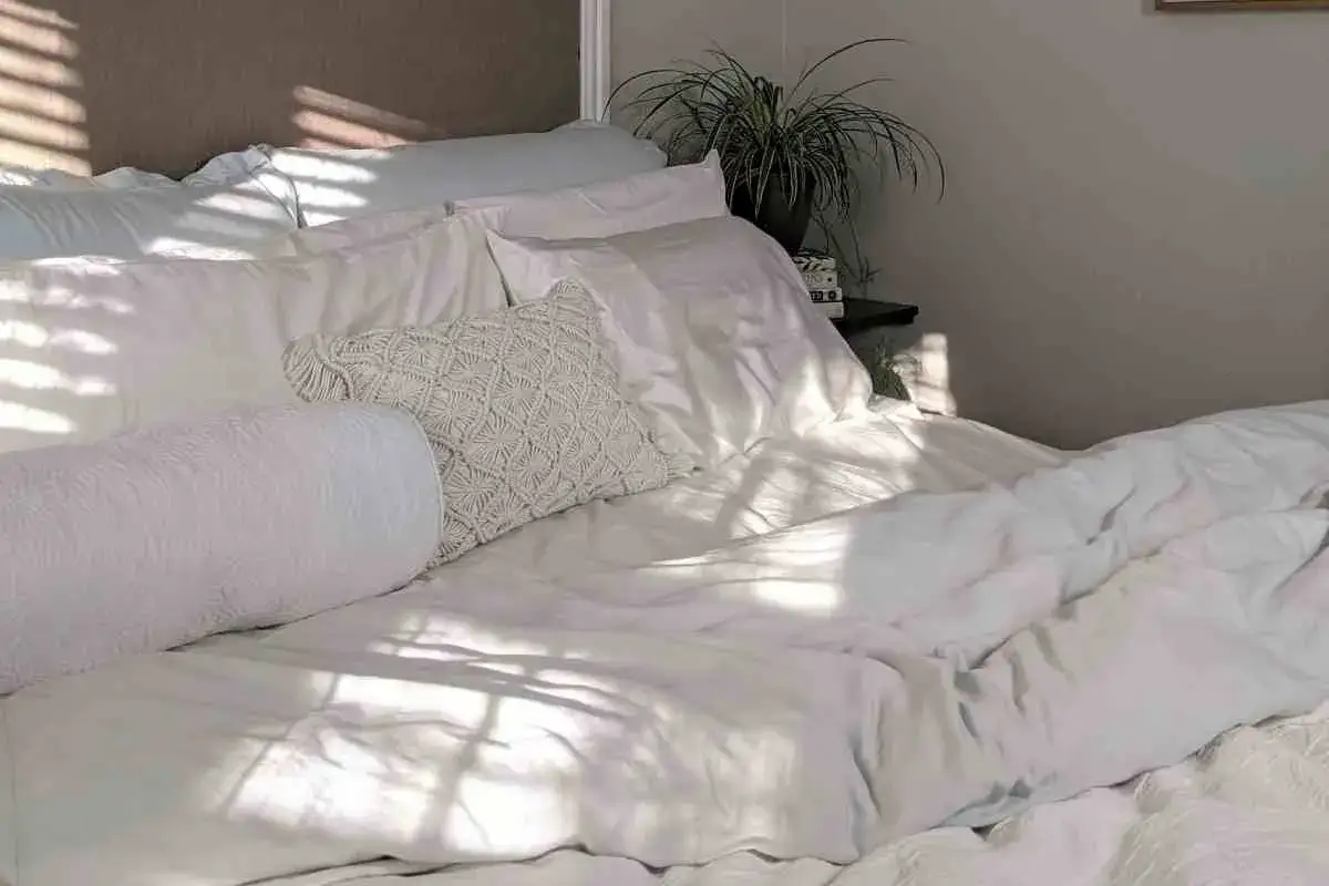 Cama blanca con almohadas y un edredón de plumas. Aprende como lavar un edredón de plumas para mantenerlo esponjoso.