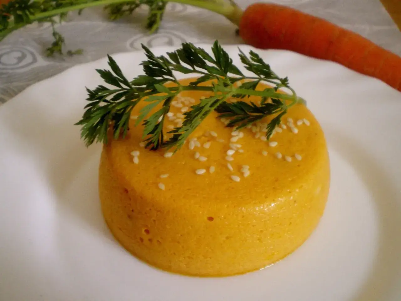Flan de carottes orange vif, parsem&eacute; de graines de s&eacute;same et garni d'une feuille de carotte.