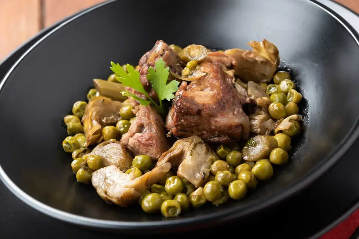 Un saporito agnello con piselli e carciofi, guarnito con prezzemolo fresco, servito in una ciotola nera.