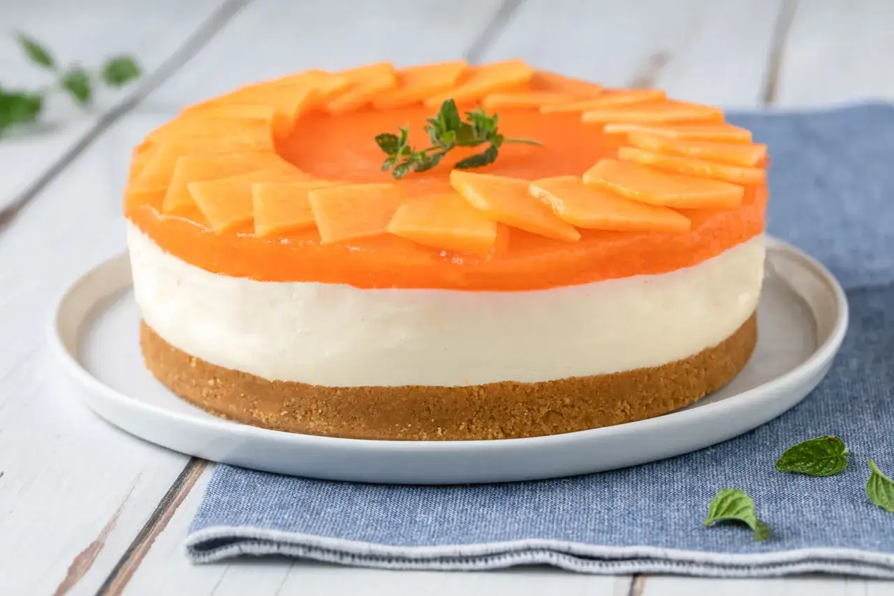 Delizioso cheesecake al melone con strati cremosi e topping di frutta fresca, decorato con menta.