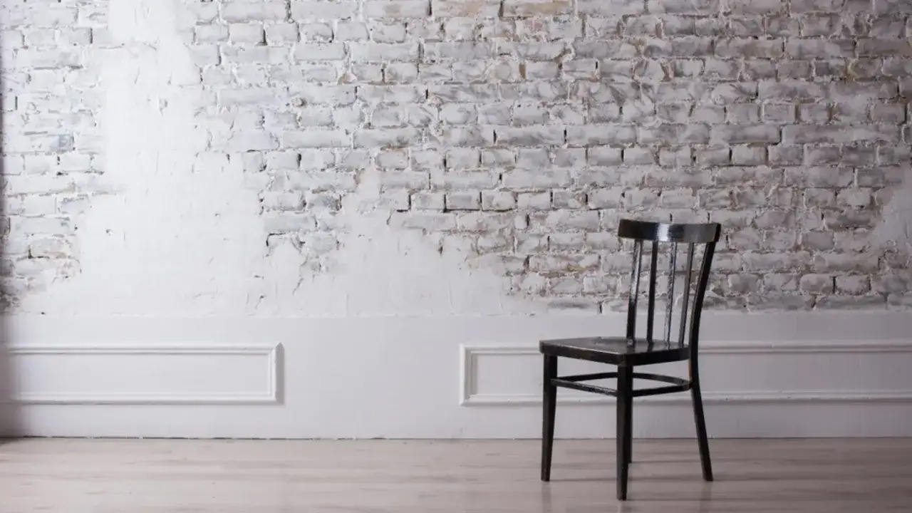 Silla negra frente a pared de ladrillos con acabado r&uacute;stico, resultado de pintar pared de piedra en blanco.