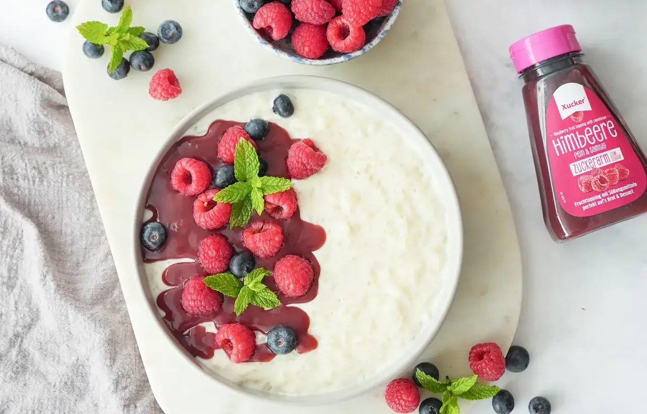 Cremiger Milchreis mit Risottoreis, garniert mit frischen Himbeeren, Blaubeeren und Minze, dazu eine Himbeersauce.