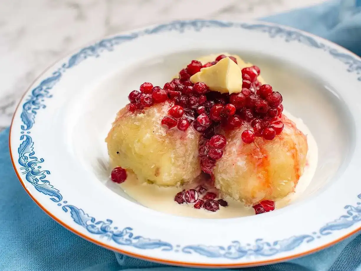 Kroppkakor recept: tv&aring; potatisbullar med lingon och sm&ouml;r i en vit tallrik med bl&aring; kant.