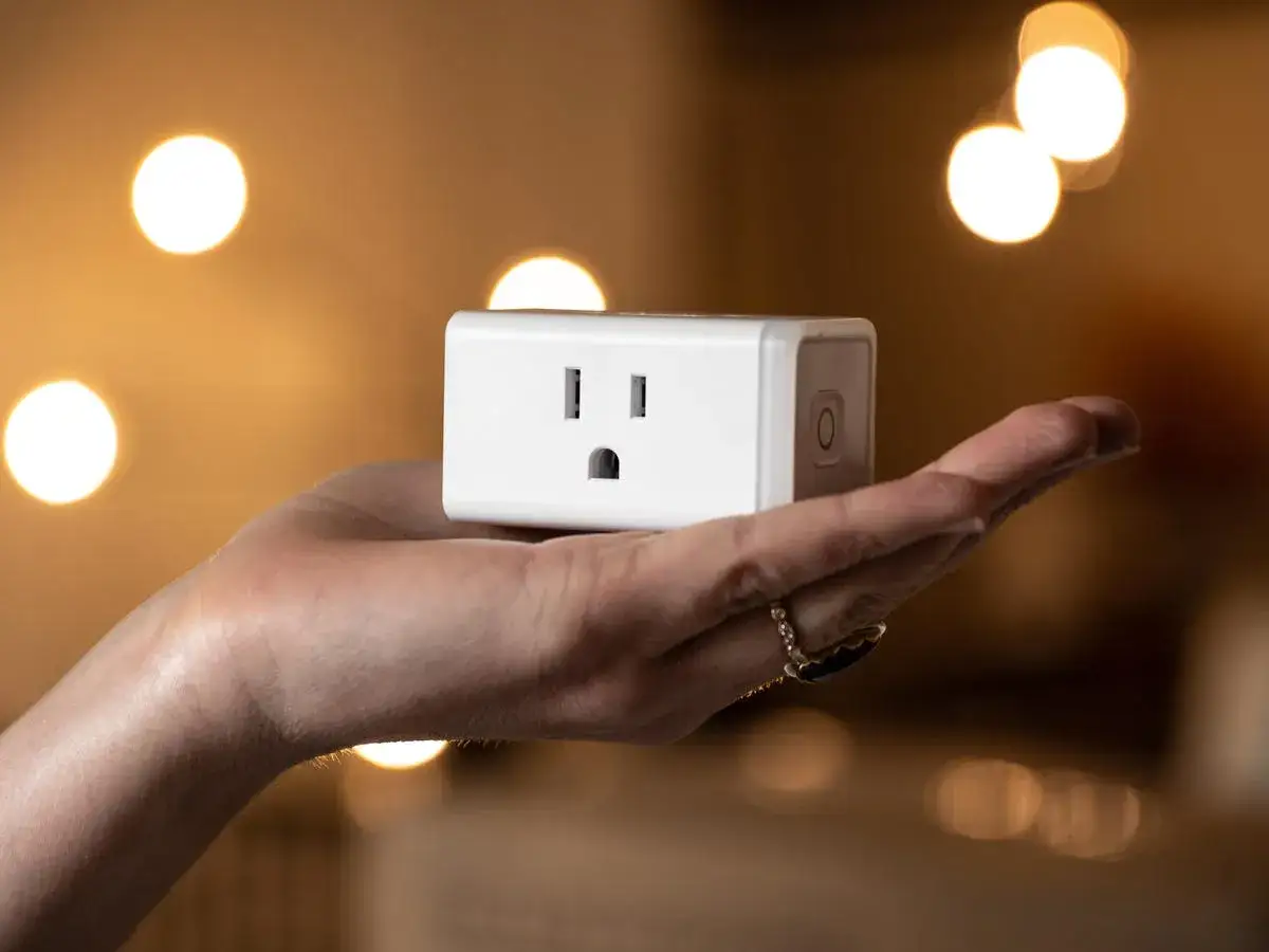Mano sostiene un enchufe inteligente blanco, listo para configurar tu hogar.