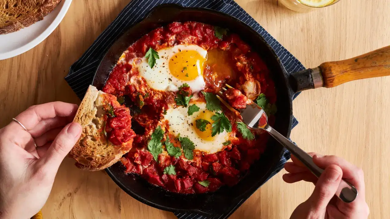 &OElig;ufs poch&eacute;s dans une sauce tomate &eacute;pic&eacute;e, parfaits pour une recette de chakchouka. Servi dans une po&ecirc;le en fonte avec du pain grill&eacute;.