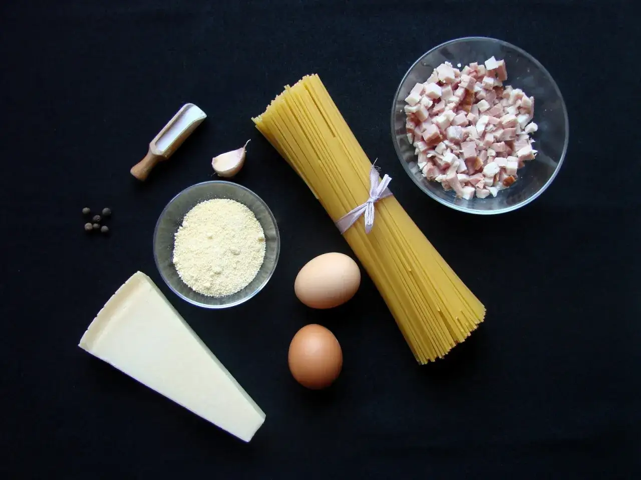 Składniki na carbonarę: makaron spaghetti, jajka, parmezan, czosnek, pieprz i pokrojony w kostkę boczek.