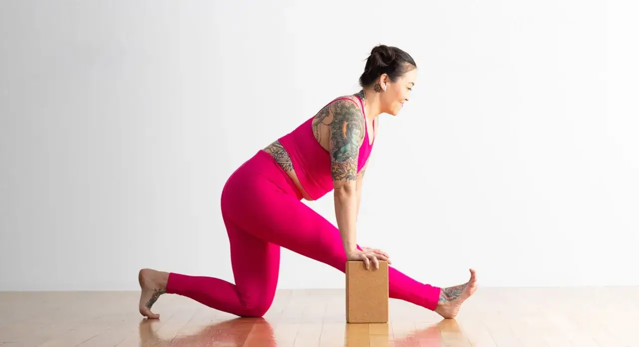 Donna in posa Ardha Hanumanasana, con un blocco yoga sotto la mano. Gamba destra tesa in avanti, ginocchio sinistro a terra.