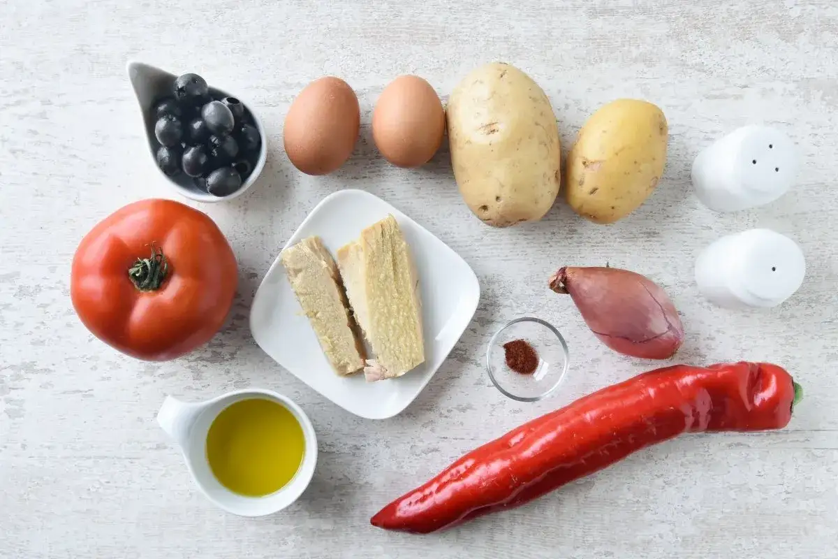 Ingredientes para una ensalada campera: patatas, huevos, tomate, pimiento rojo, aceitunas, cebolla, atún, aceite, sal y pimentón.