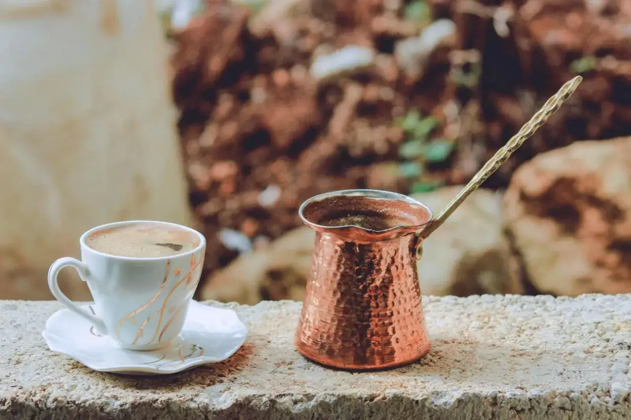 Caff&egrave; turco pronto in tazza, accanto al bricco di rame. Scopri come fare il caff&egrave; turco senza cezve per un'esperienza autentica.