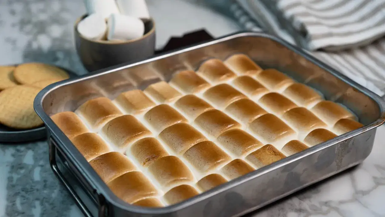 S'mores i ugn, gyllene marshmallows som sm&auml;lter &ouml;ver choklad och kex i en ugnsform. En h&auml;rlig dessert som v&auml;ntar p&aring; att avnjutas.