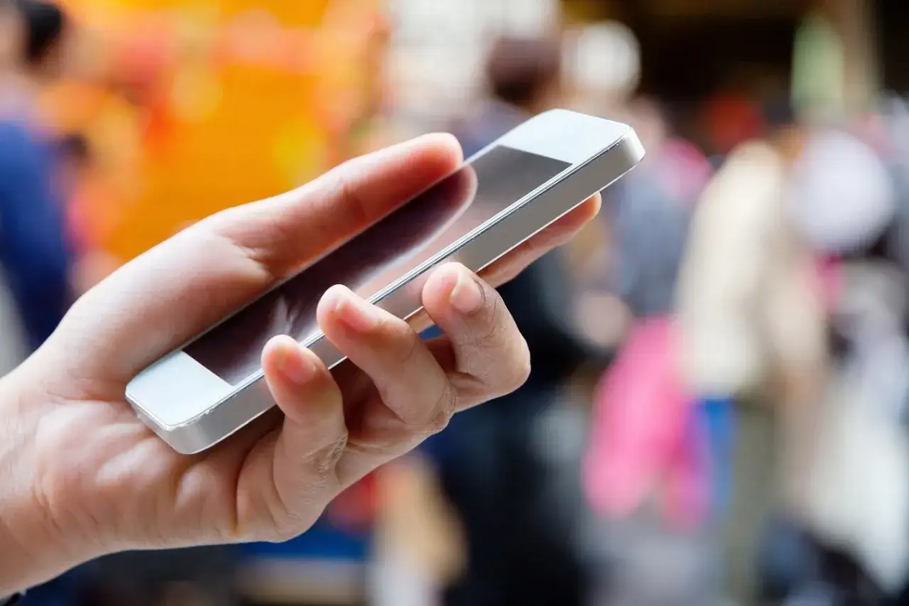 Dłoń trzyma smartfon, gotowa do wykonania telefonu. To Twój pierwszy krok, jak zapytać się o pracę przez telefon.