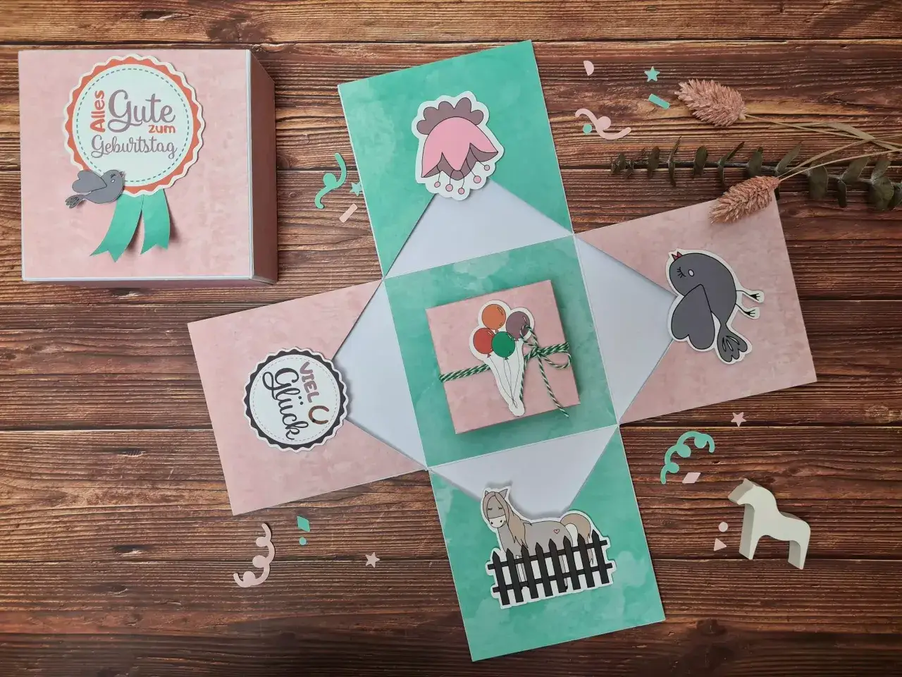 Eine liebevoll gestaltete Geschenkbox basteln: Rosa und mintgrüne Klappen mit süßen Motiven wie Vögeln, Ballons und einem Pferd.