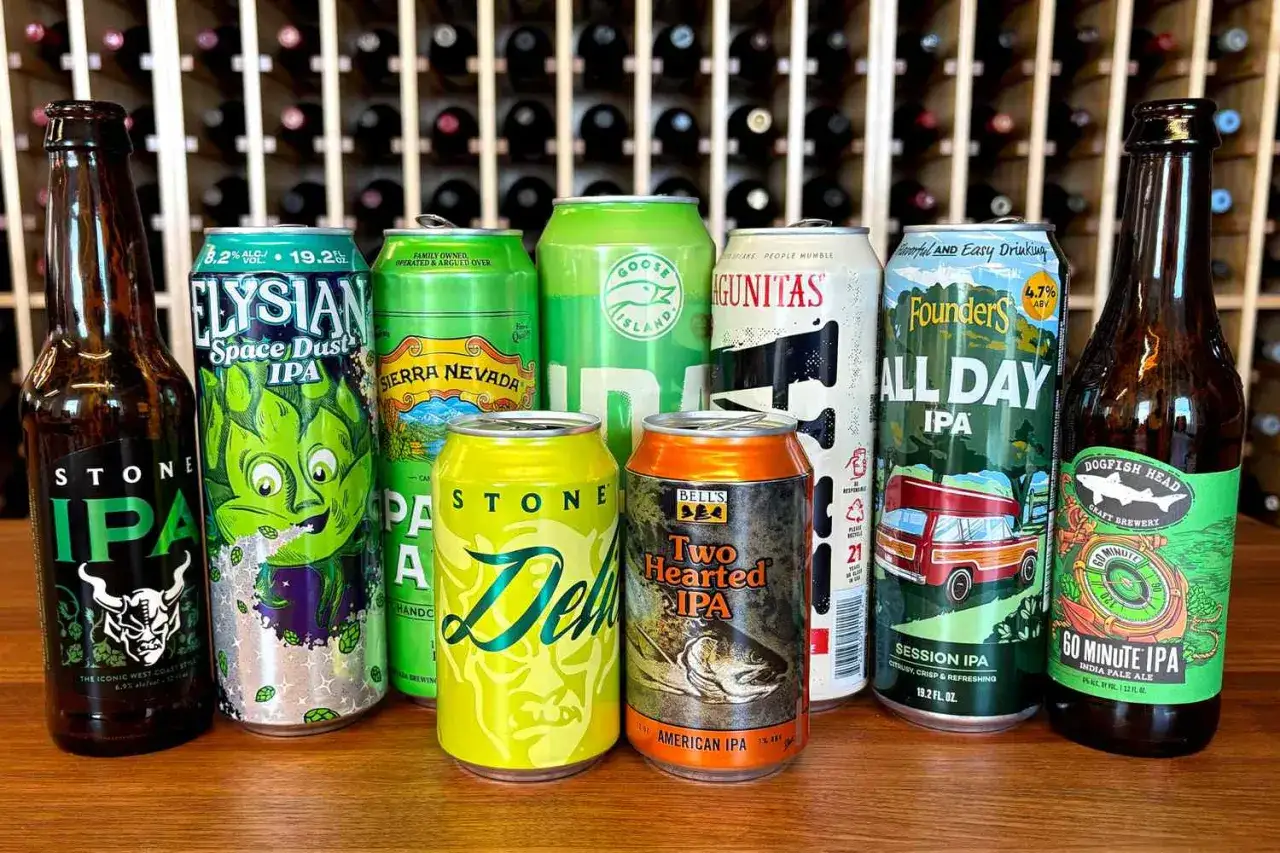Różnorodne puszki i butelki piwa IPA, w tym Stone IPA, Elysian Space Dust IPA, Sierra Nevada, Founders All Day IPA i Dogfish Head 60 Minute IPA, stoją na drewnianym blacie.