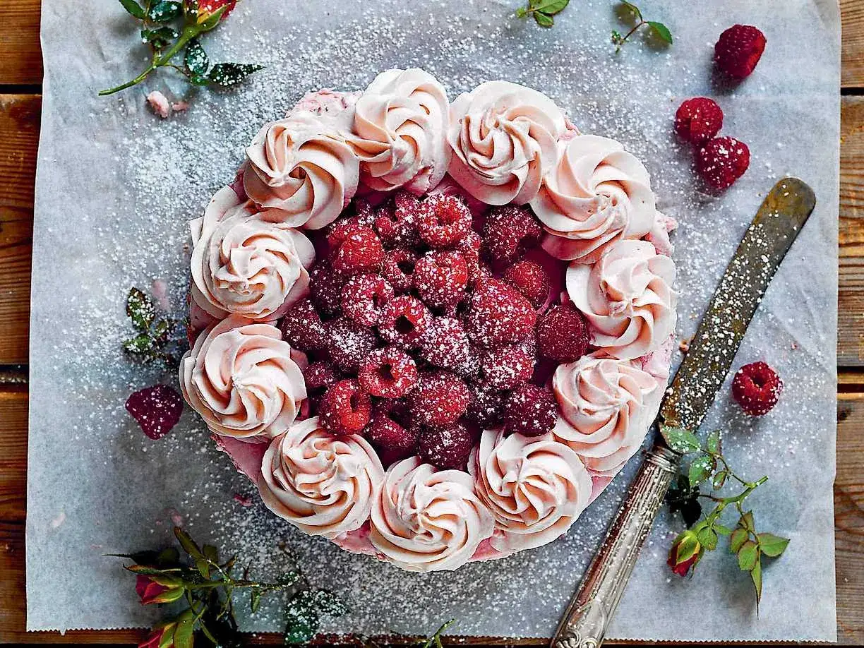 En vacker vit choklad tårta dekorerad med rosa frosting och färska hallon. Pudrad med florsocker.