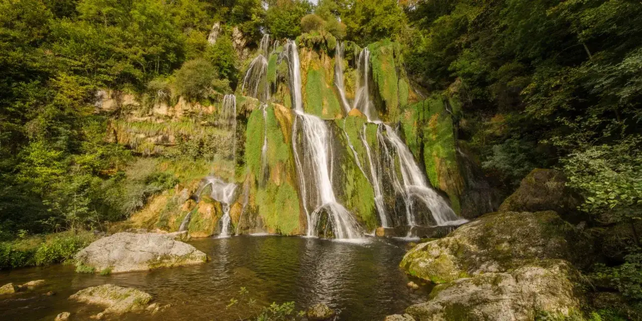 La cascade de Luizet, un rideau d'eau blanc tombant sur des rochers verdoyants, se jette dans un bassin sombre.