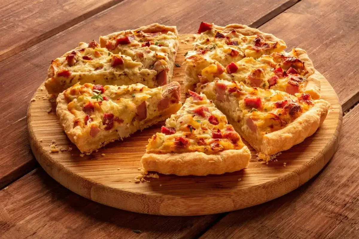 Fette di torta salata patate e salsiccia dorata e invitante, servite su un tagliere di legno rustico.