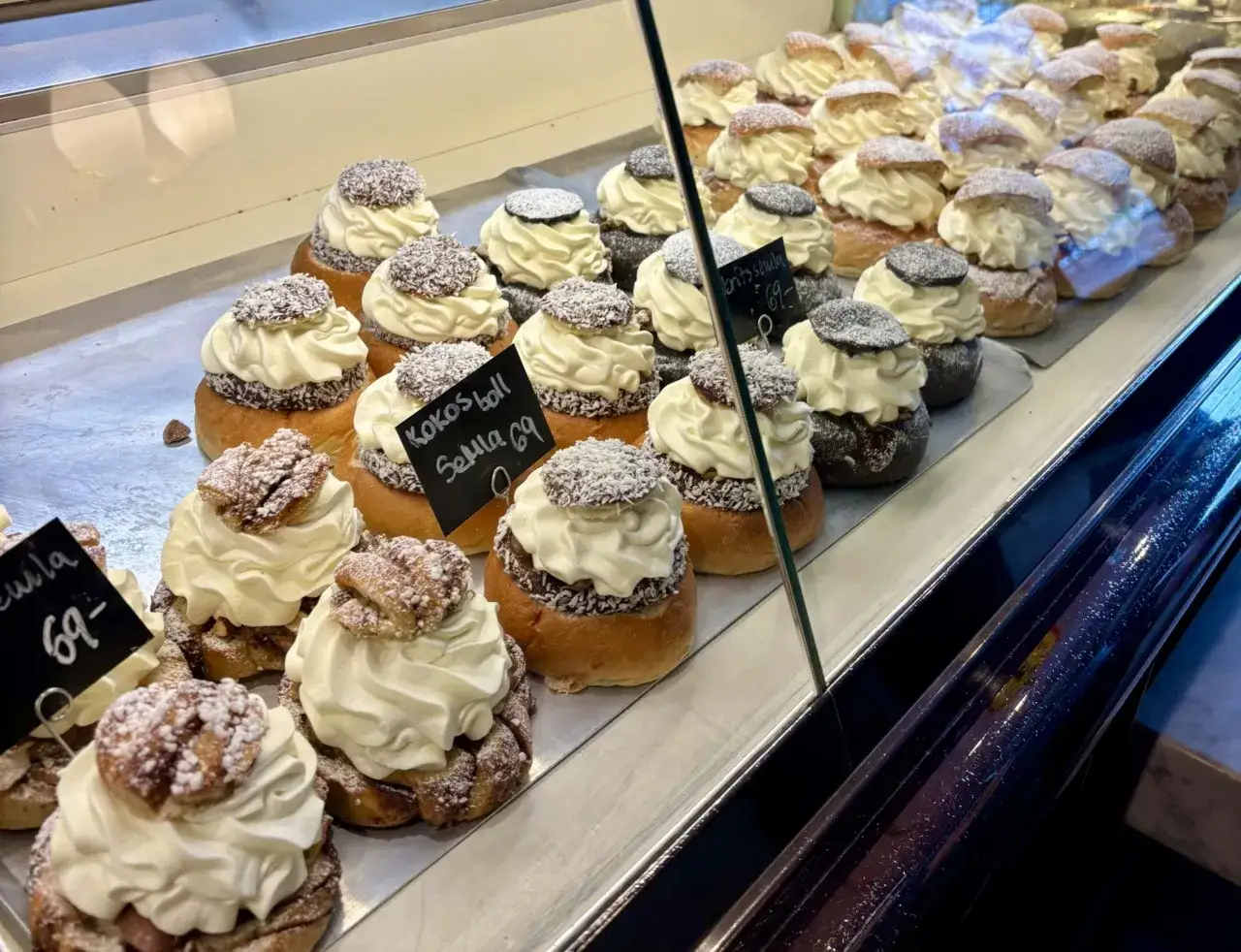 Rader av semlor med vispgrädde och strössel. En skylt visar