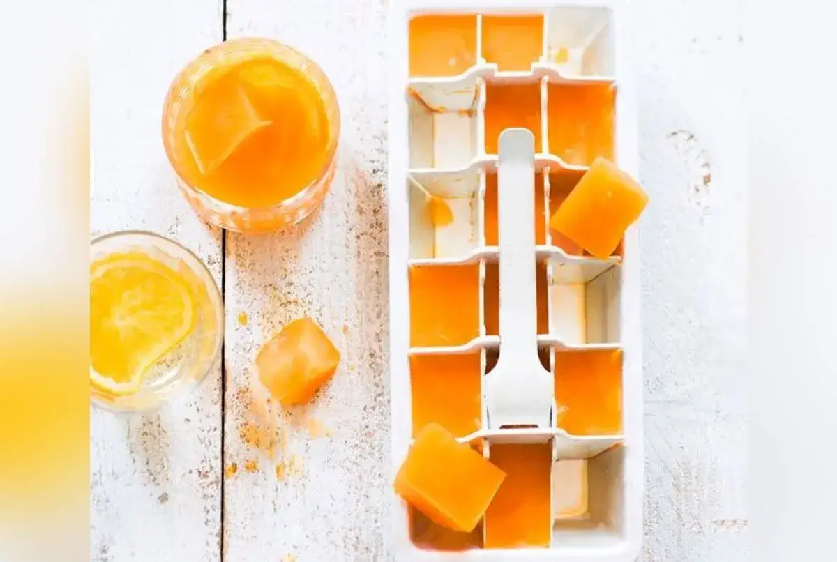 Gla&ccedil;ons orange vif dans un bac &agrave; gla&ccedil;ons, pr&ecirc;ts pour une recette spritz rafra&icirc;chissante. Un verre avec des gla&ccedil;ons et une tranche d'orange &agrave; c&ocirc;t&eacute;.