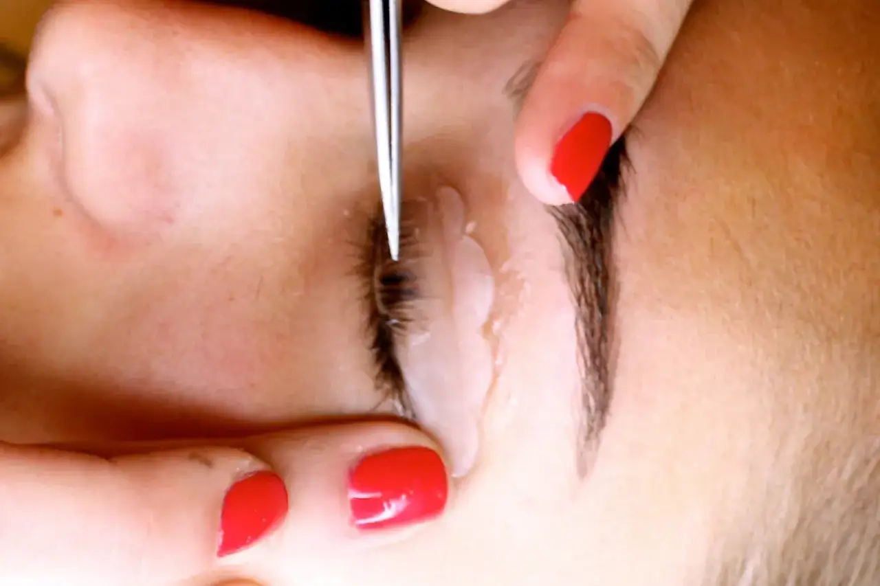 Wimpern biegen ohne Wimpernzange: Eine Hand mit roten Nägeln hält ein kleines Werkzeug, das die Wimpern formt.