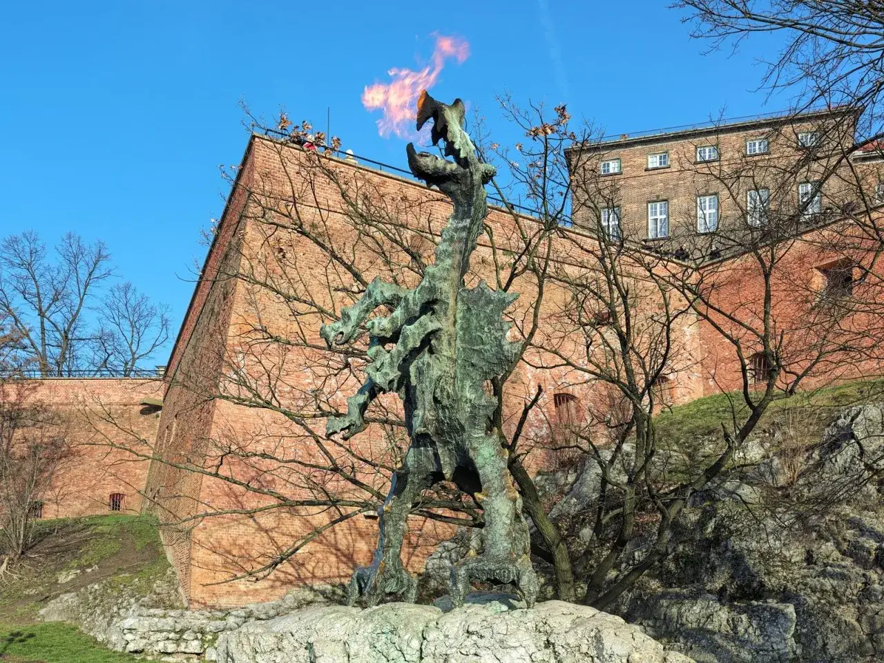 Smok Wawelski ziejący ogniem, żywa legenda Krakowa, stoi przed ceglanymi murami Wawelu.