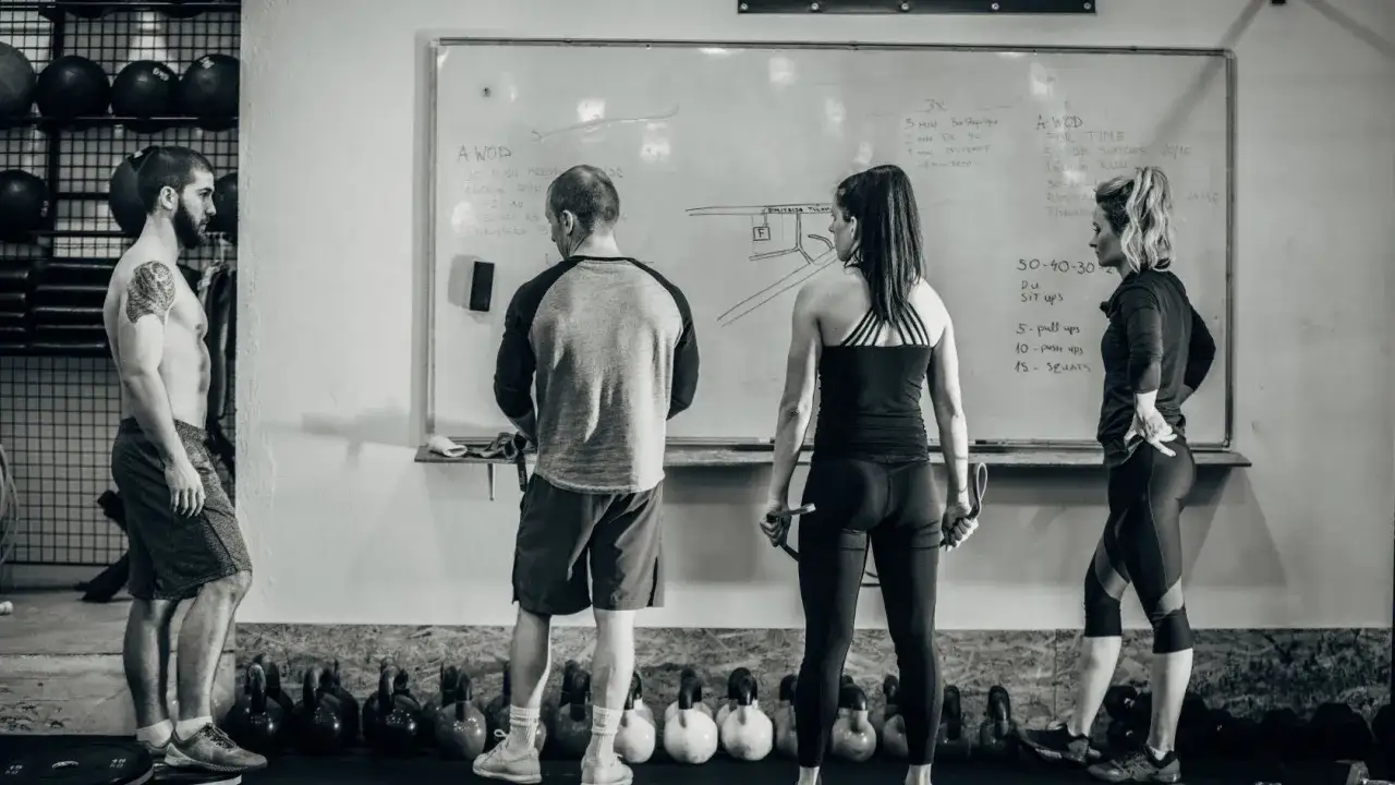 Trening na redukcji: ile razy w tygodniu cardio? Grupa os&oacute;b analizuje plan treningowy na tablicy w siłowni.