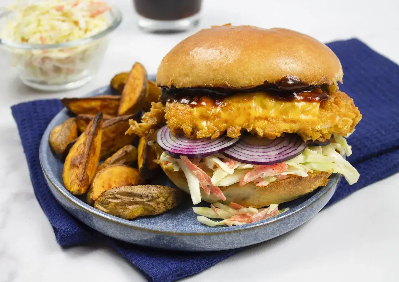 Burger z chrupiącym kurczakiem, serem, czerwoną cebulą i surówką coleslaw, podany z pieczonymi ziemniakami. Idealny sos do chikkera podkreśla smak.