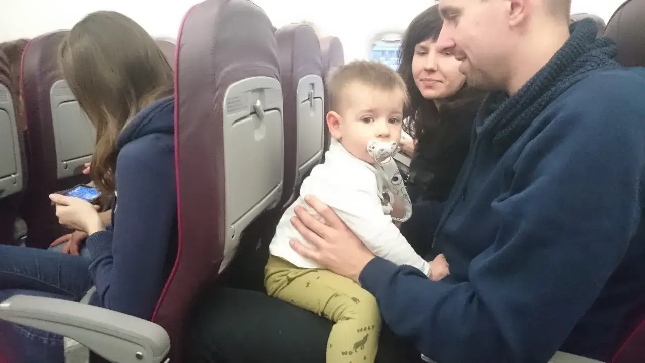 Małe dziecko z Wizz Air fotelik samochodowy na kolanach ojca w samolocie.
