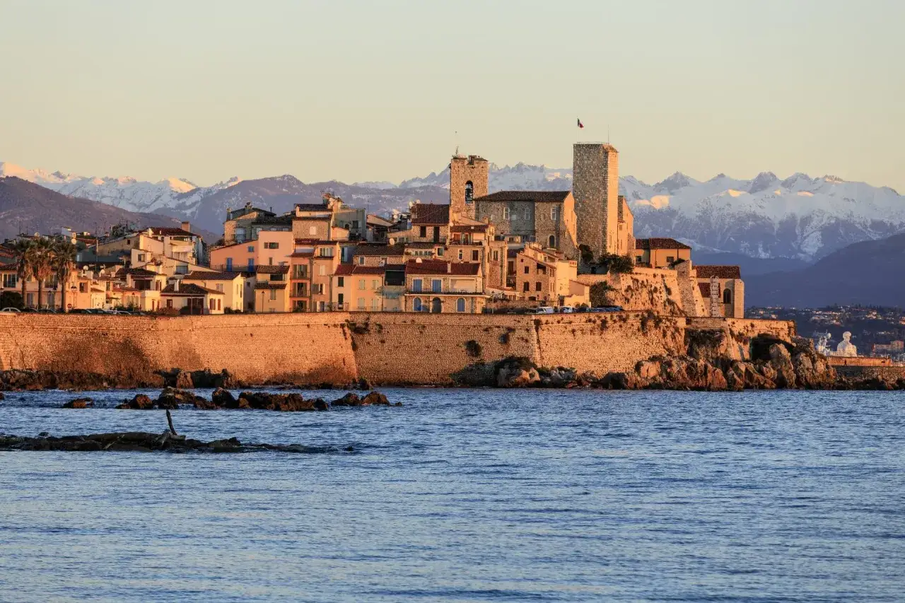 El casco antiguo de Antibes, Francia, se alza sobre el mar Mediterr&aacute;neo, con monta&ntilde;as nevadas al fondo.