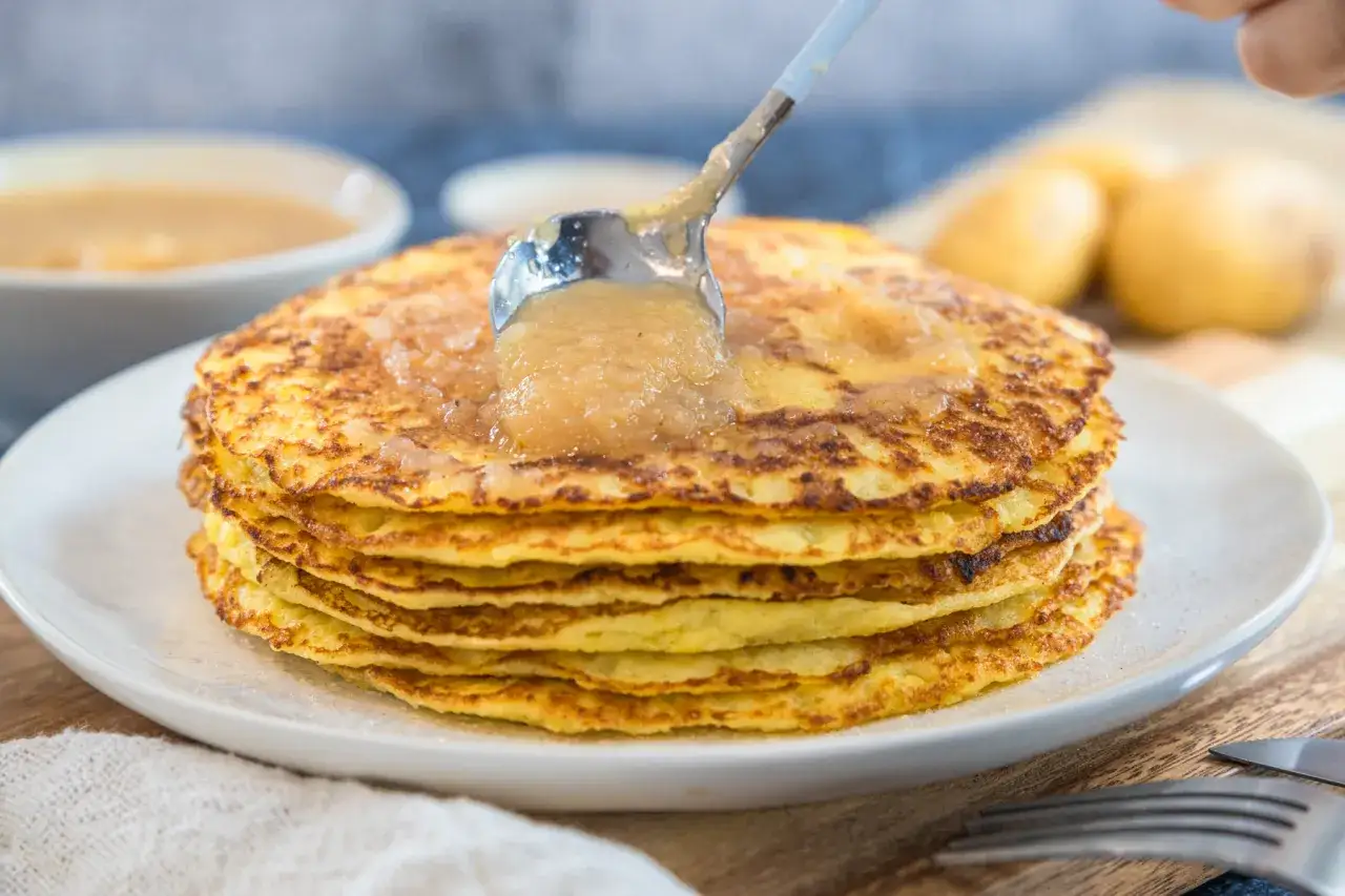 Ein Stapel goldbrauner Kartoffelpuffer, zubereitet im Thermomix, wird mit Apfelmus beträufelt. Lecker!