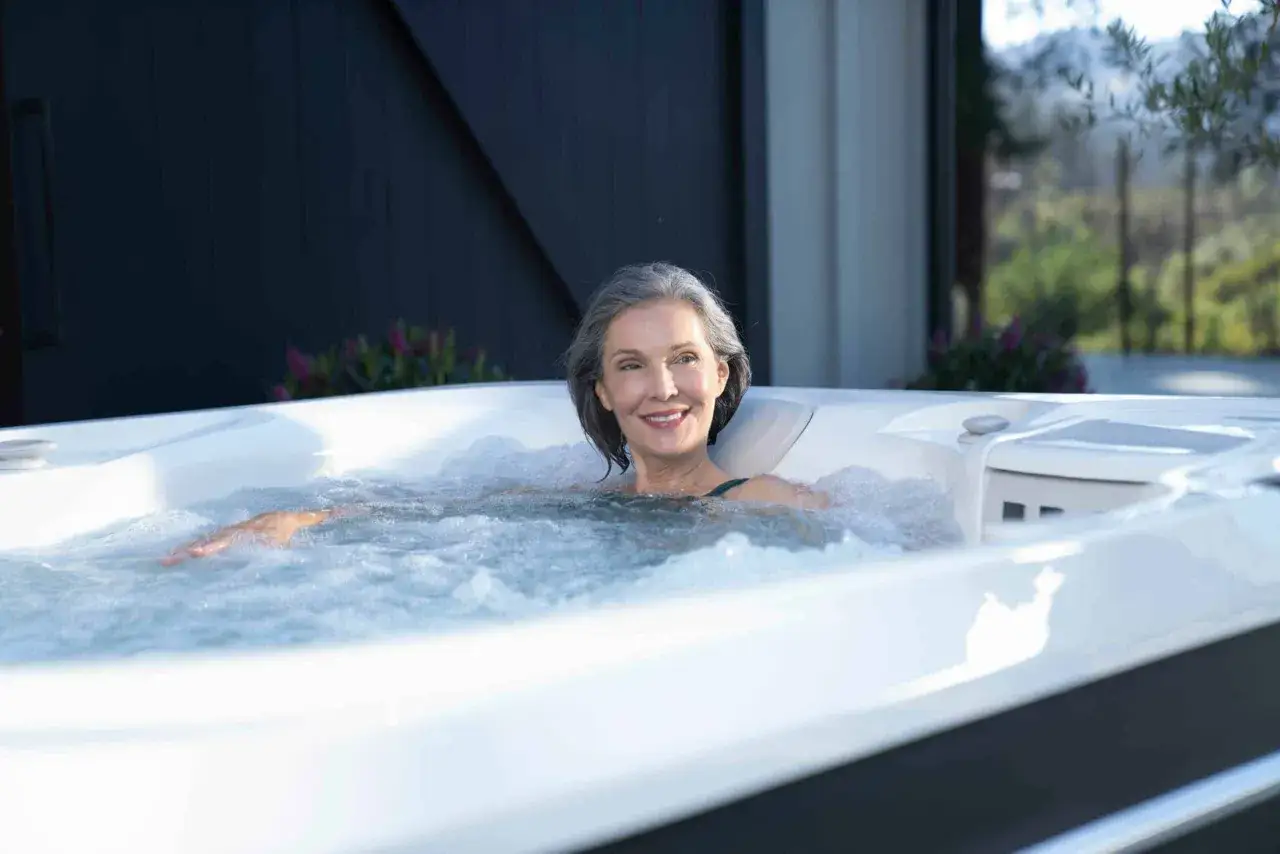 Uśmiechnięta kobieta w jacuzzi, relaksująca się w bąbelkach. Czy jacuzzi odchudza? To pytanie zadaje sobie wiele os&oacute;b, szukając relaksu i formy.