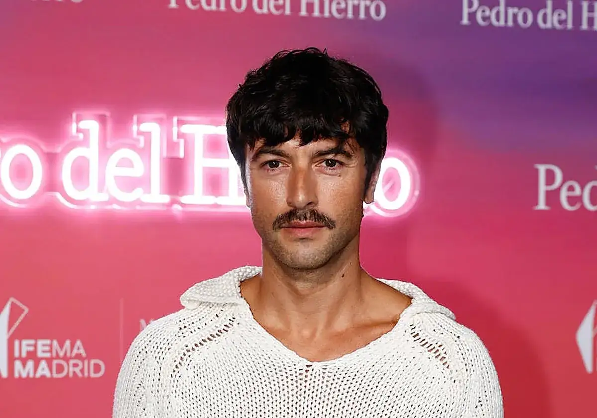 Hombre con un estiloso bigote, perfecto para Movember, luce un su&eacute;ter blanco de punto.