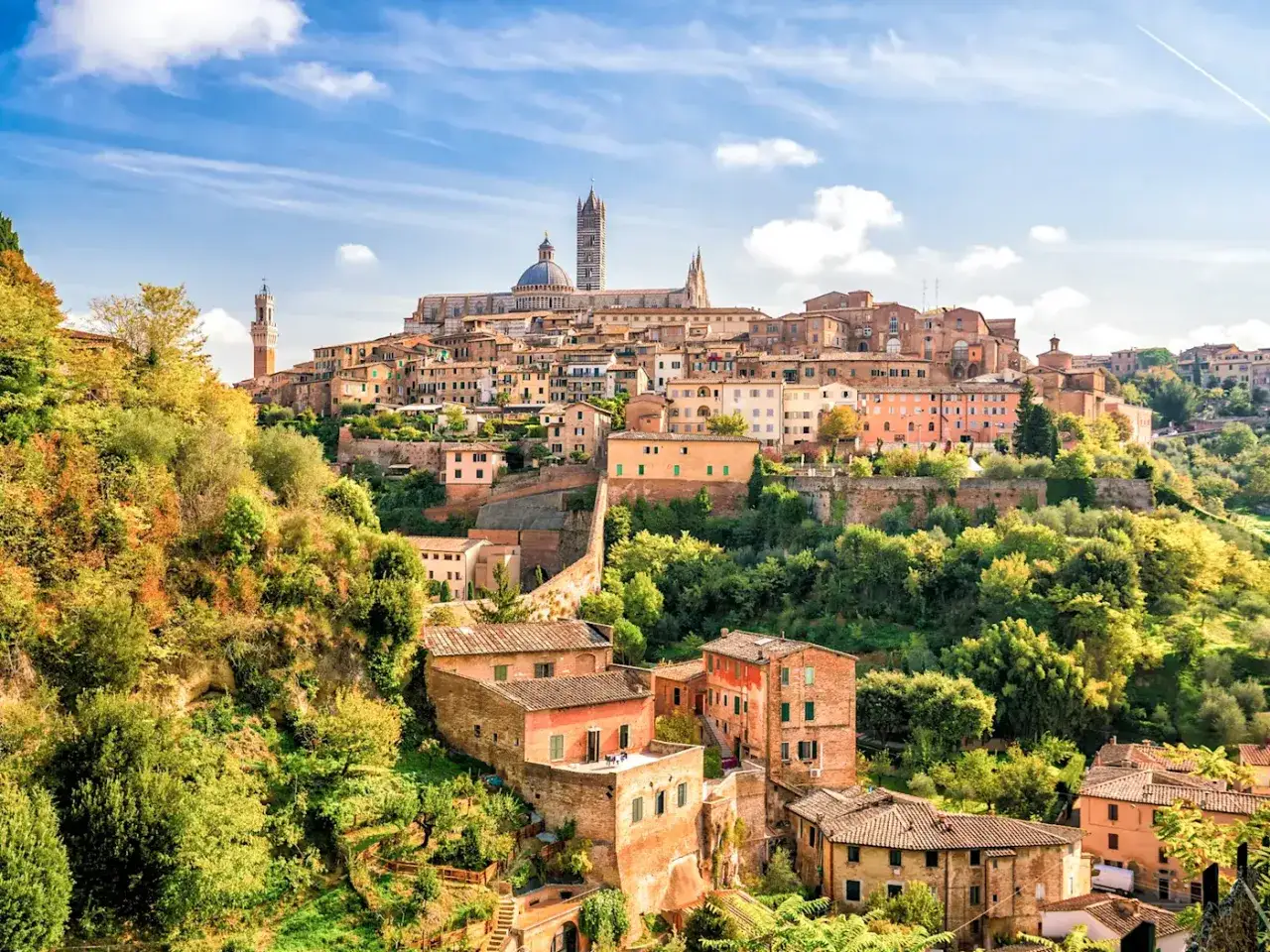 Vue panoramique de Sienne, une ville médiévale perchée sur une colline en Toscane, Italie. Les toits de tuiles rouges et les tours se dressent au milieu d'une végétation luxuriante.