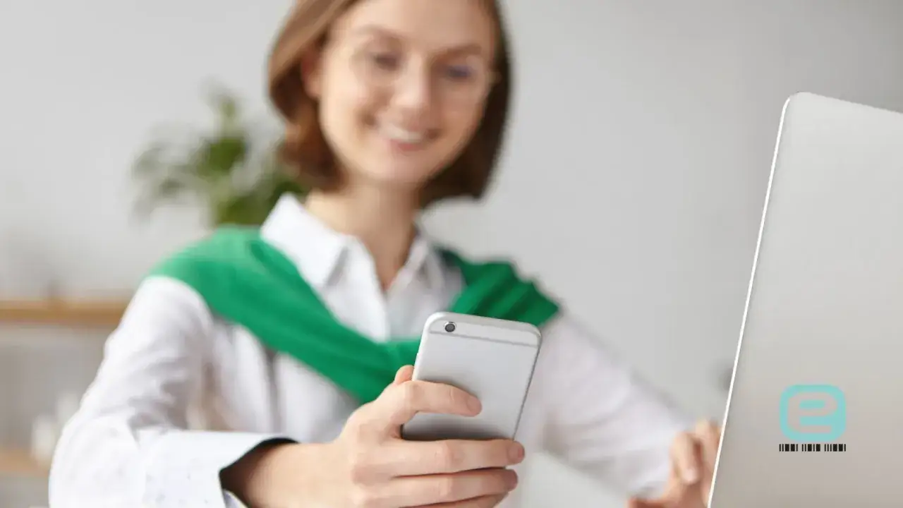 Uśmiechnięta kobieta z telefonem w dłoni, korzystająca z możliwości zwolnienia lekarskiego online.