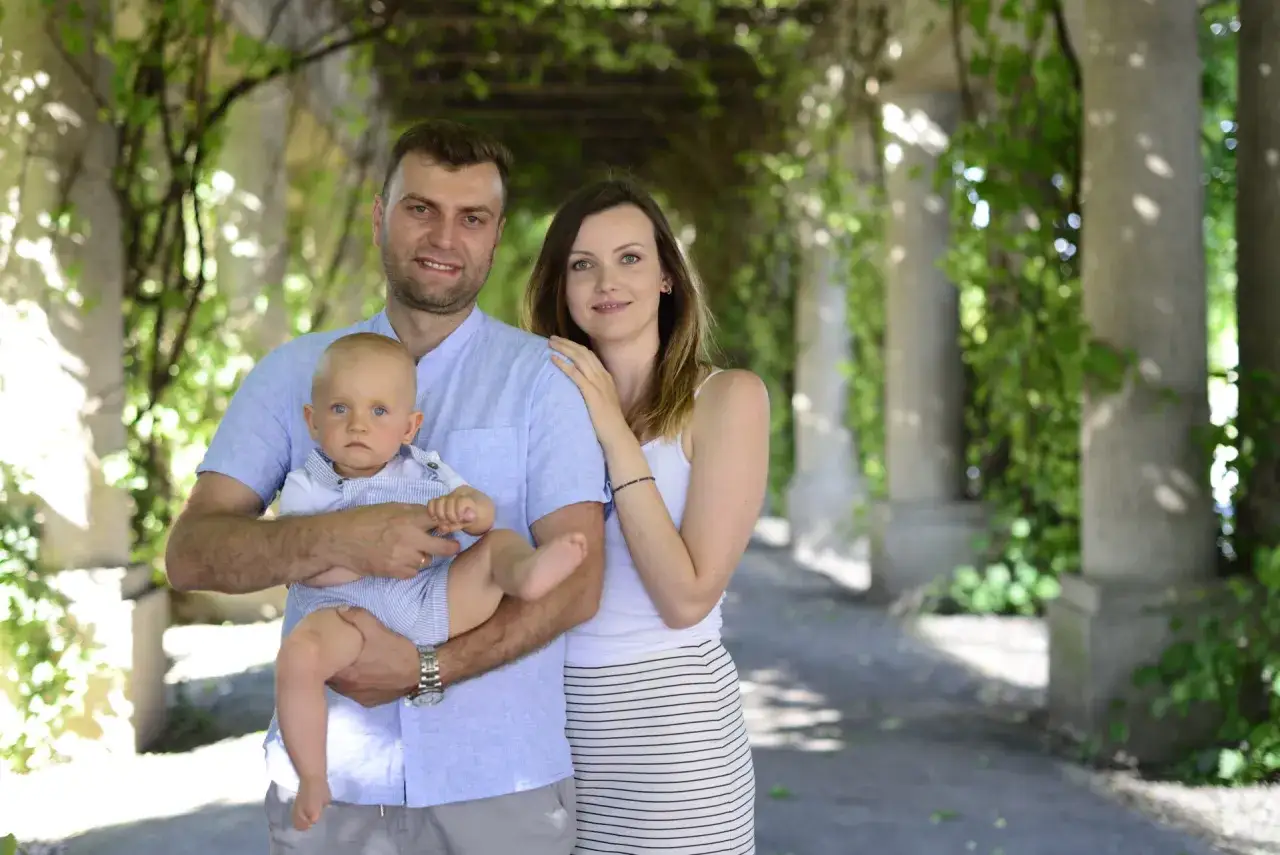 Rodzina na sesji zdjęciowej. Ojciec trzyma dziecko, matka obejmuje męża. Wskazówki, jak ubrać dziecko na sesję zdjęciową.
