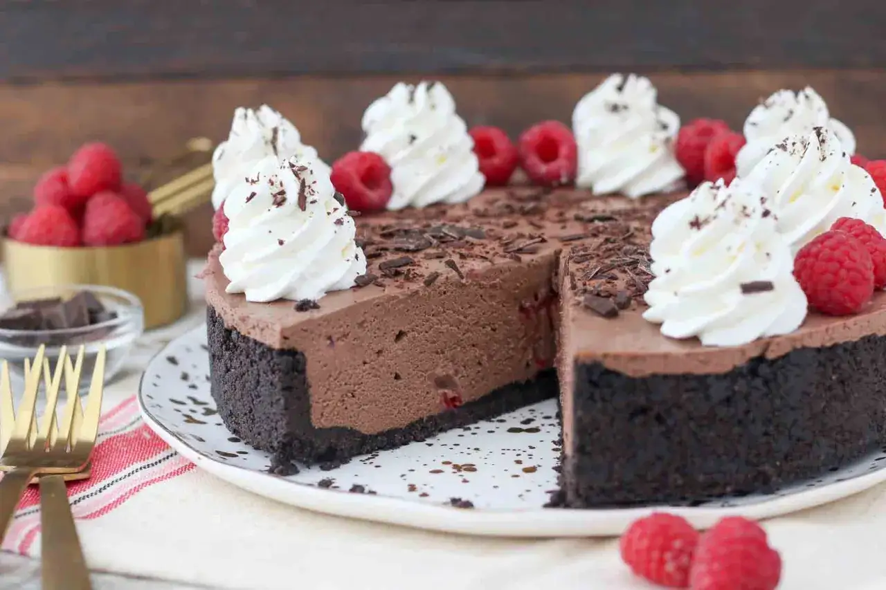 Délicieux gâteau sans cuisson au chocolat et aux framboises, garni de crème fouettée et de copeaux de chocolat.