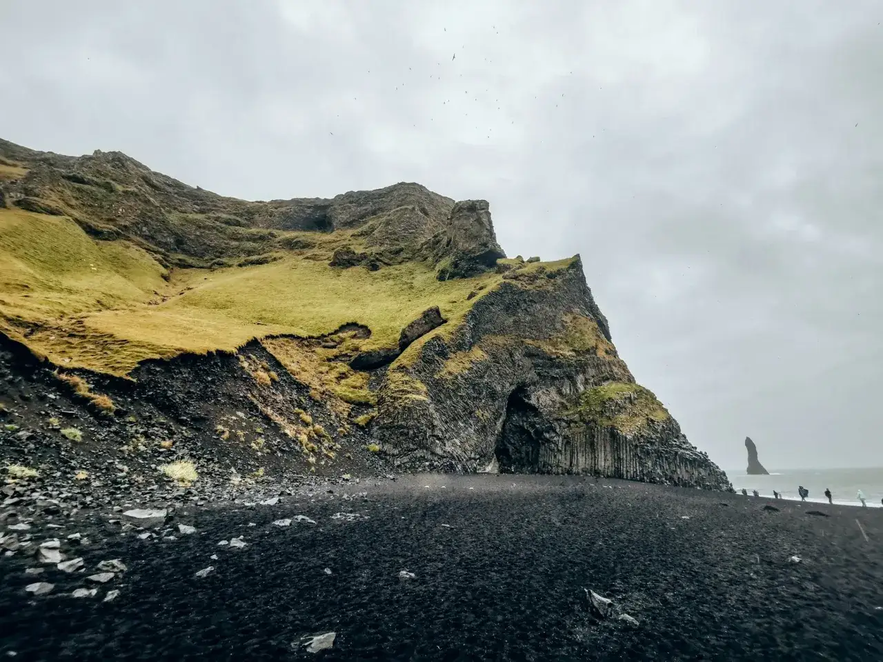 Majestatyczna czarna plaża Islandia z bazaltowymi kolumnami i jaskinią w klifie. Na horyzoncie widać samotną skałę.
