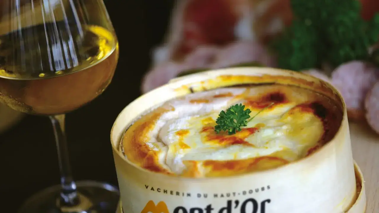Un Mont d'Or cr&eacute;meux, dor&eacute; au four, avec une touche de persil, &agrave; c&ocirc;t&eacute; d'un verre de vin blanc.