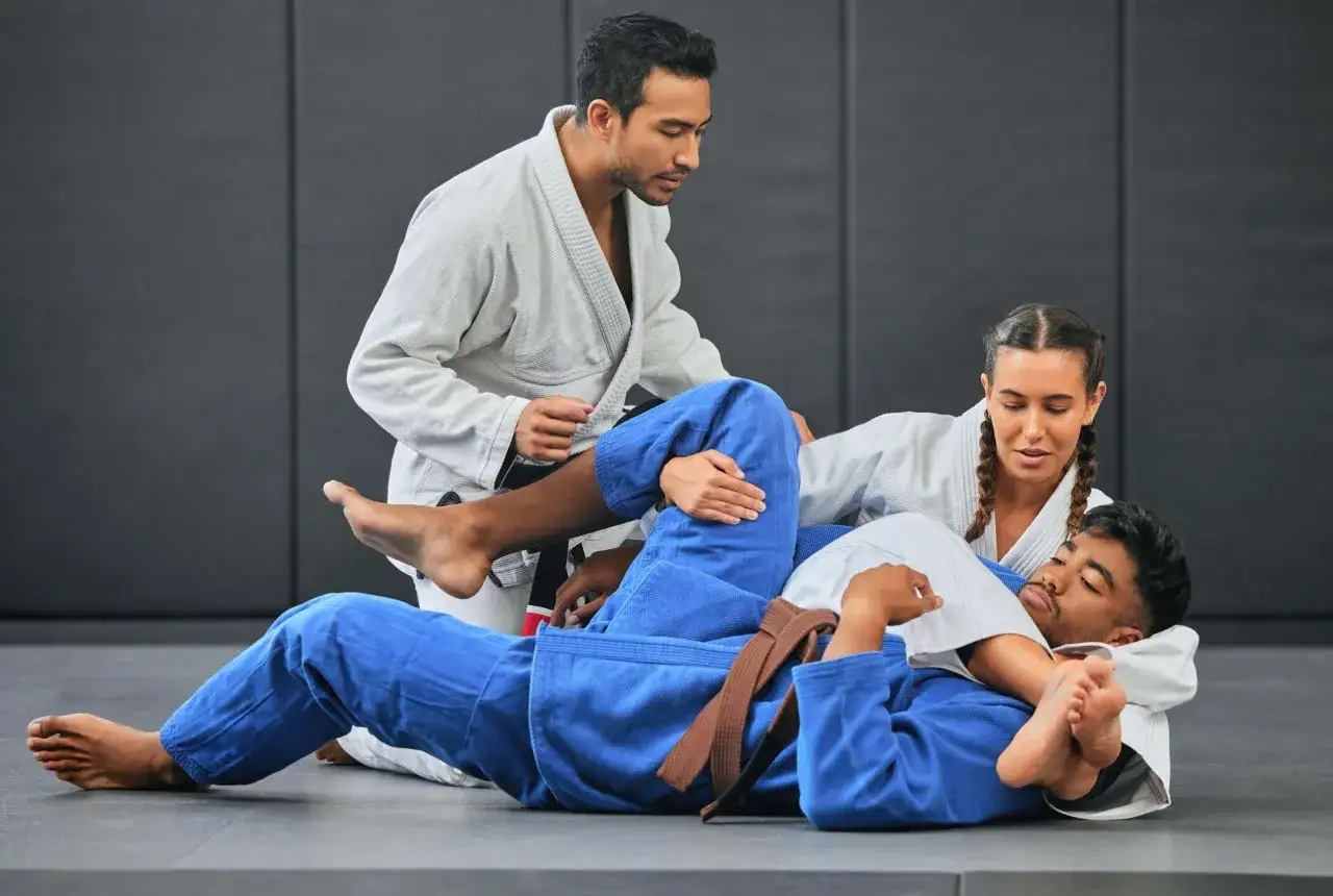 Tr&auml;nare instruerar tv&aring; elever i ju jitsu. En elev ligger p&aring; rygg medan den andra sitter &ouml;ver honom.