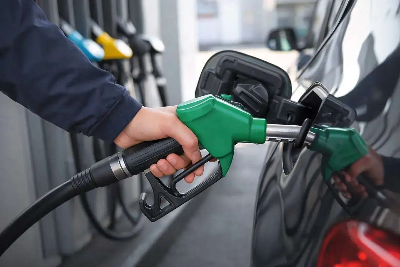 Ręka trzyma zielony pistolet dystrybutora, tankując **diesel paliwo** do samochodu. W tle widać inne dystrybutory.