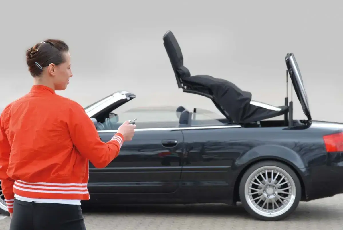 Frau öffnet das Verdeck ihres schwarzen Audi A4 B6 Cabrio mit dem Schlüssel.