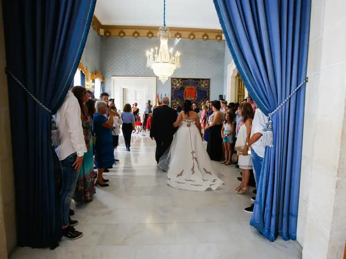 Novios caminan hacia el altar, rodeados de invitados. Una escena que evoca las ventajas de casarse por lo civil: sencillez y uni&oacute;n.
